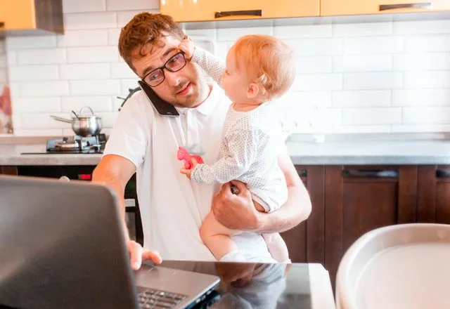 un freelance avec son bébé dans les bras au téléphone