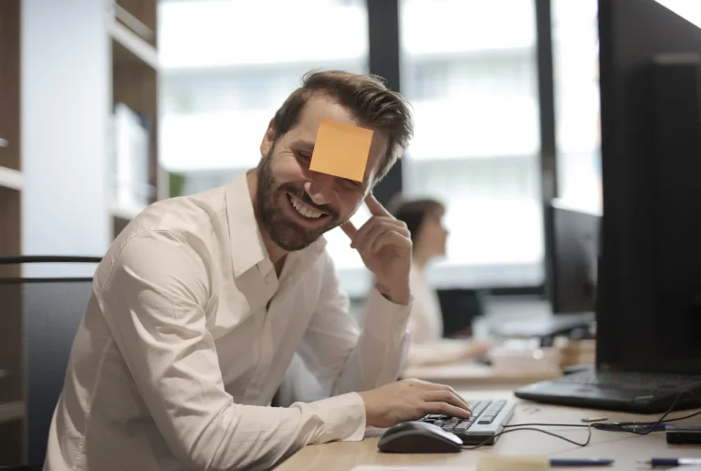 un homme qui rigole au boulot avec un post it sur le front