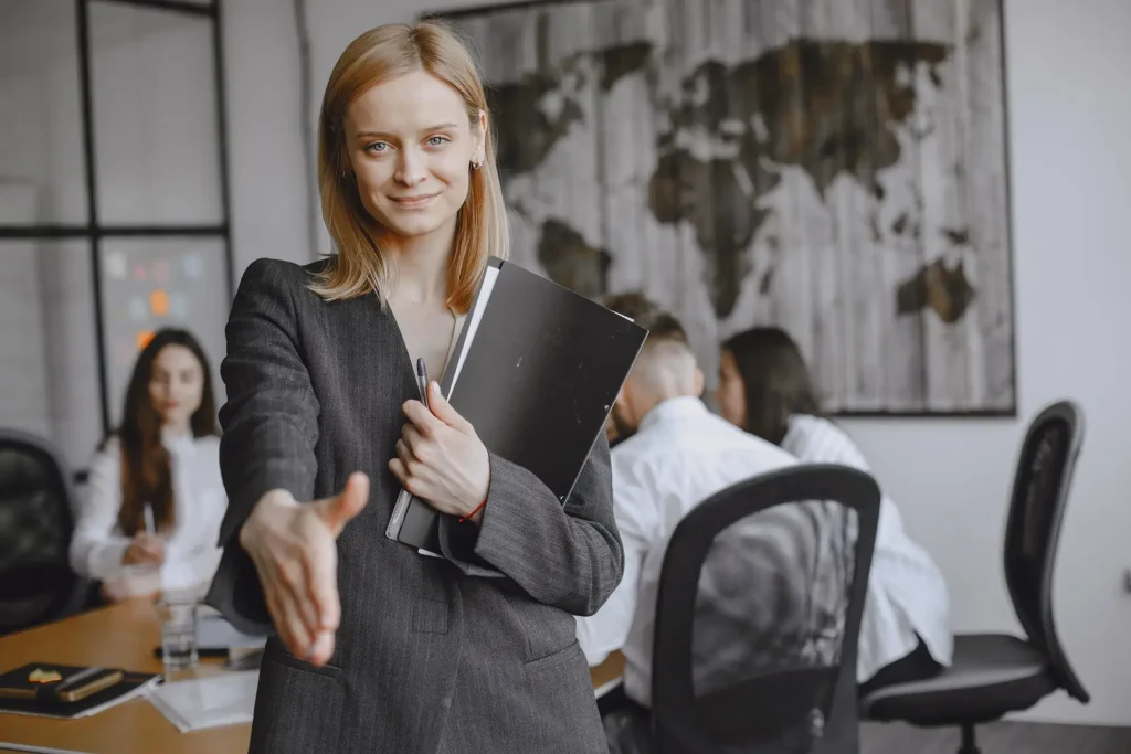 une femme en réunion qui tend la main vers l'objectif